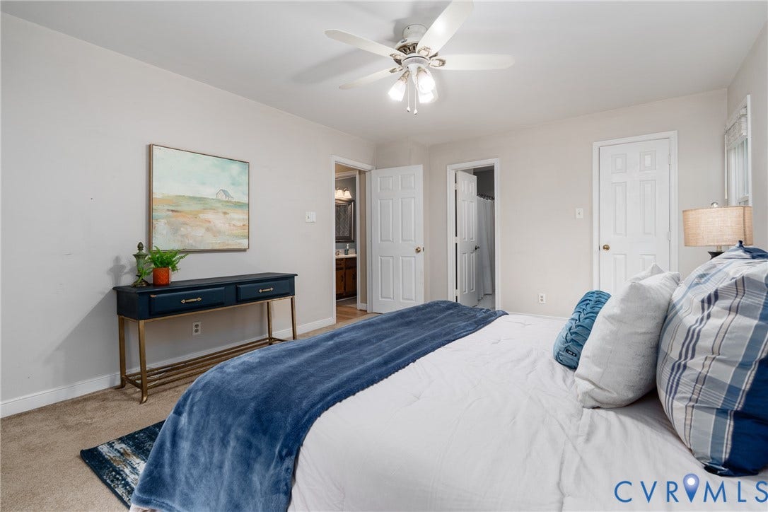 Neutral tone wall paint, white trim, ceiling fan with light fixture, carpeted flooring, and white paneled doors.