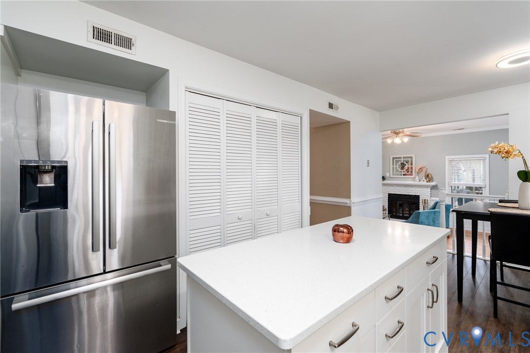 Stainless steel French door refrigerator, white kitchen island with integrated storage, white louvered bifold doors, recessed lighting, and wood-finish flooring.
