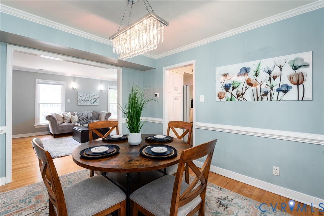 Dining area featuring a crystal chandelier, crown molding, chair rail molding, and wood-finish flooring.