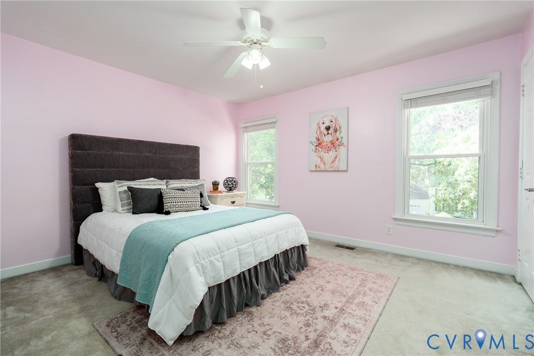 White ceiling fan, two windows with white trim, light-colored carpeting, and a built-in white door.