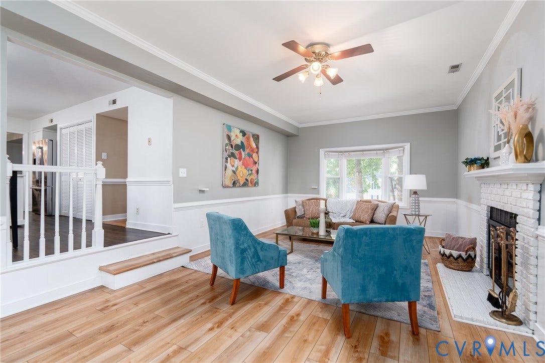 Bright living area featuring wood-finish flooring, a white brick fireplace with a hearth, and a ceiling fan