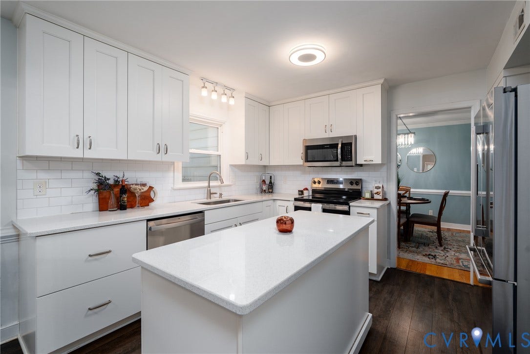 White kitchen cabinetry, stainless steel appliances, central island with solid surface countertop, subway tile backsplash, and dark wood-finish flooring.