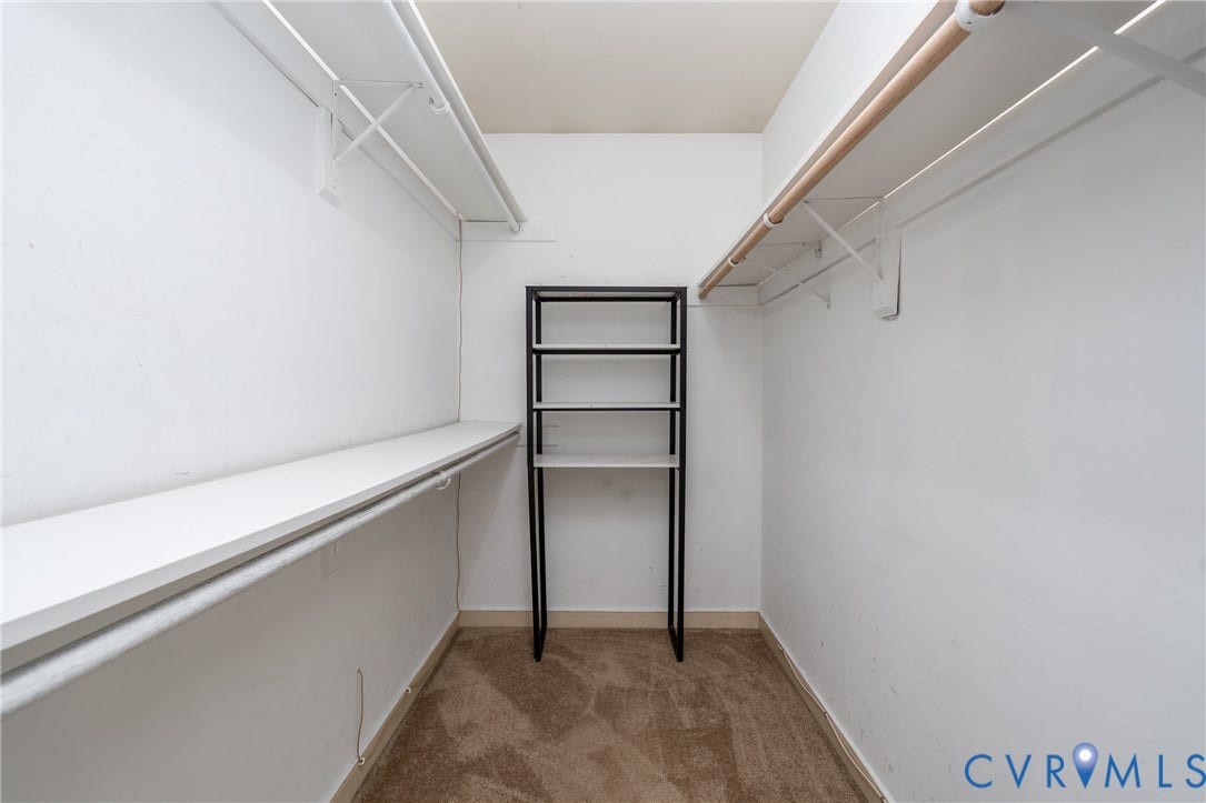 Walk-in closet featuring built-in shelving, a wooden clothing rod, and neutral-toned carpeting.