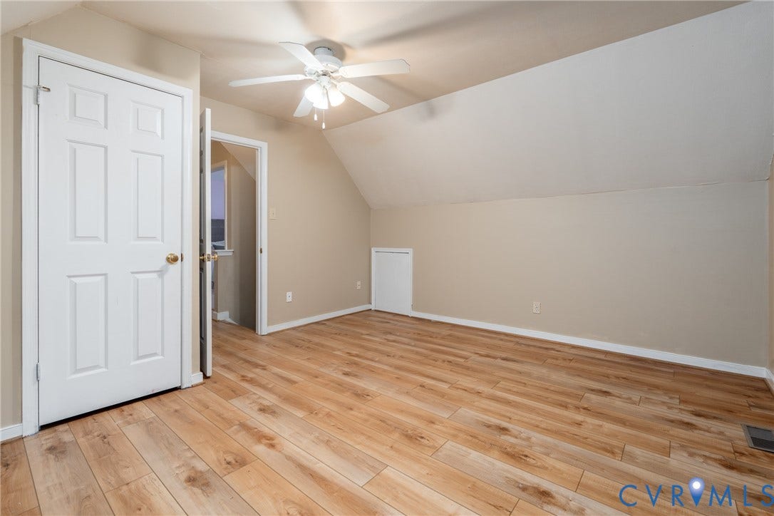 Wood-finish flooring, white paneled doors, ceiling fan with integrated lighting, and sloped ceiling