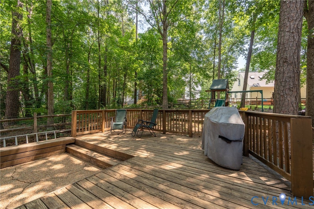 Multi-level wood deck with wood baluster railing and integrated steps, surrounded by mature trees.