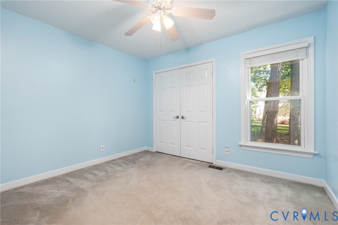Light blue painted walls, gray carpeting, dual white bi-fold closet doors, and a window with white trim.