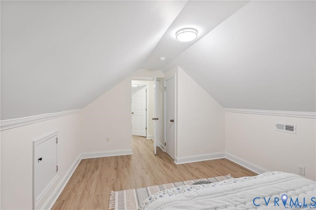 Angled ceiling with a flush-mount light fixture, wood-finish flooring, and white walls