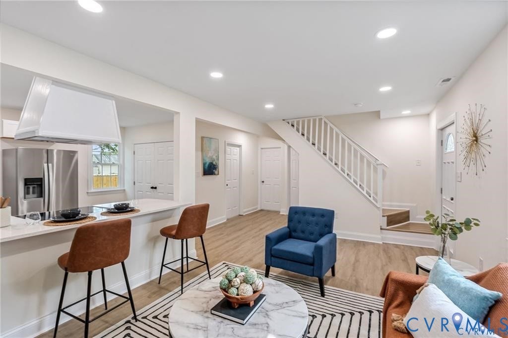 Open-concept living space featuring wood-finish flooring, recessed lighting, and a white staircase
