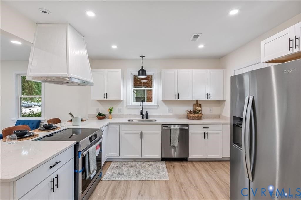 Kitchen featuring white cabinetry, light-toned countertops, stainless steel appliances, wood-finish flooring, and recessed lighting