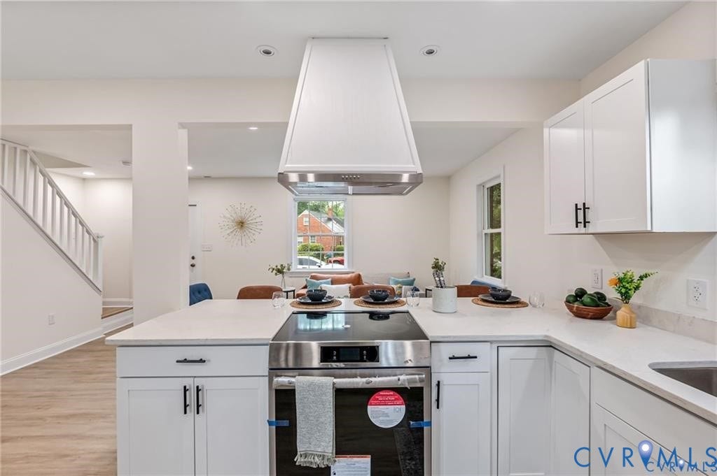 White cabinetry, light countertops, wood-finish flooring, stainless steel range, and a decorative range hood
