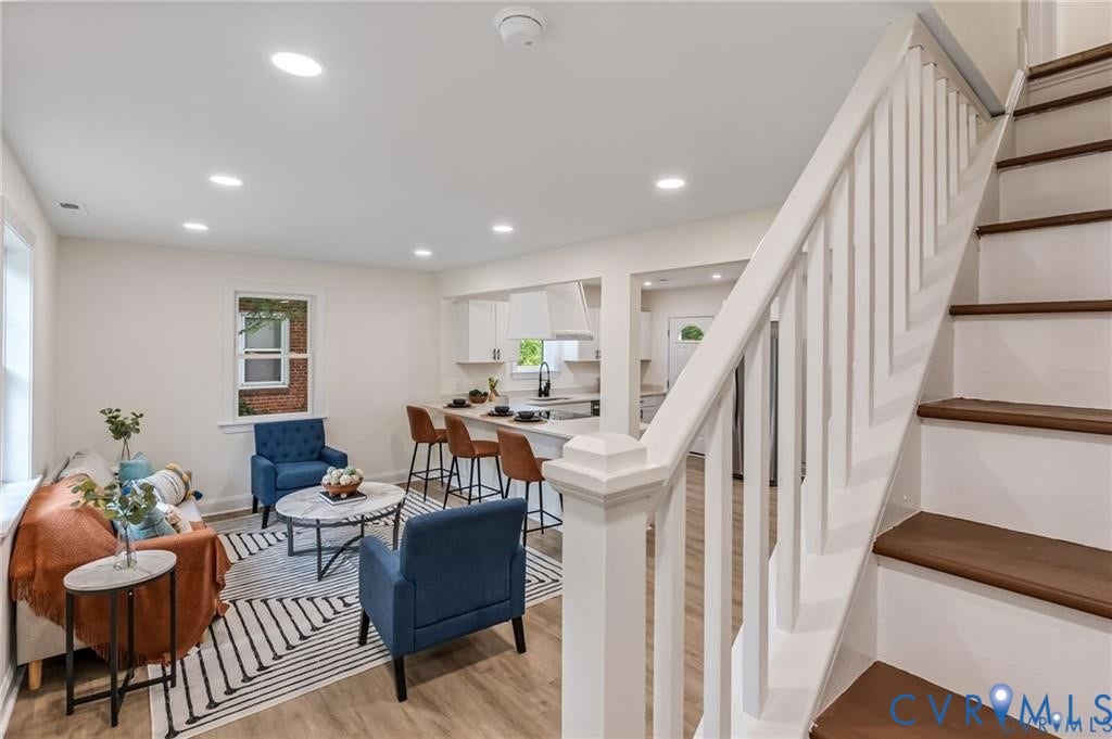 Recessed lighting, wood-finish flooring, white kitchen cabinetry, a kitchen island with seating, and a staircase with white risers and wood treads