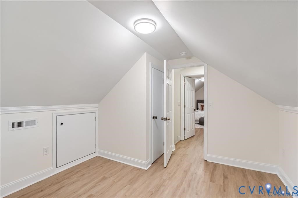 Sloped ceilings, wood-finish flooring, white trim, and a flush-mount ceiling light