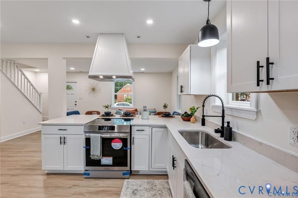 Kitchen featuring white shaker cabinetry, an integrated stainless steel oven, a coordinating range hood, a stainless steel sink with a matte black gooseneck faucet, and light-colored countertops