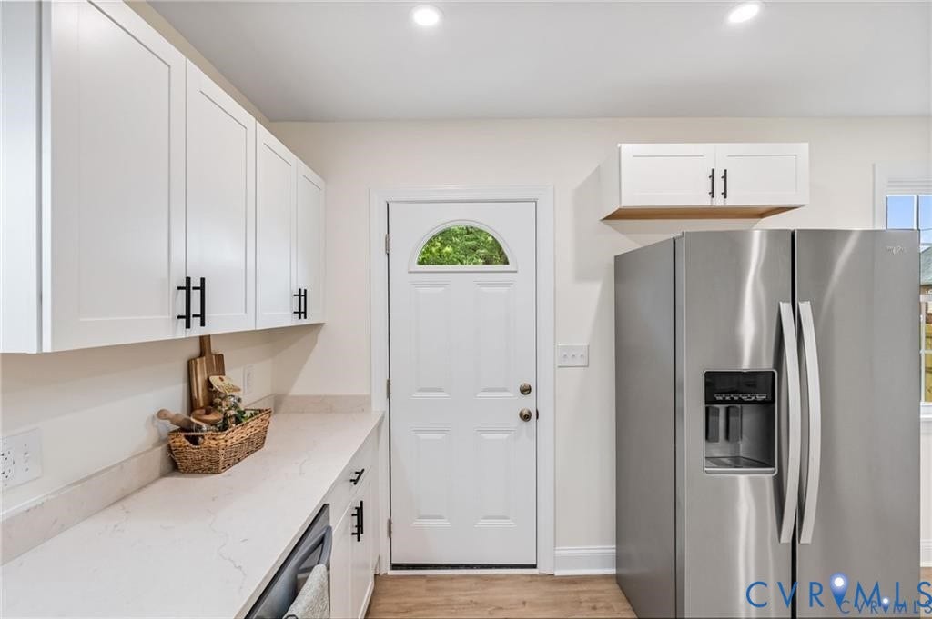 White shaker-style cabinetry with matte black hardware, light-toned countertops, a side-by-side stainless steel refrigerator, and wood-finish flooring