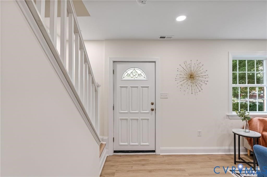 White paneled entry door with decorative glass, wood-finish flooring, white trim throughout, and a multi-pane window
