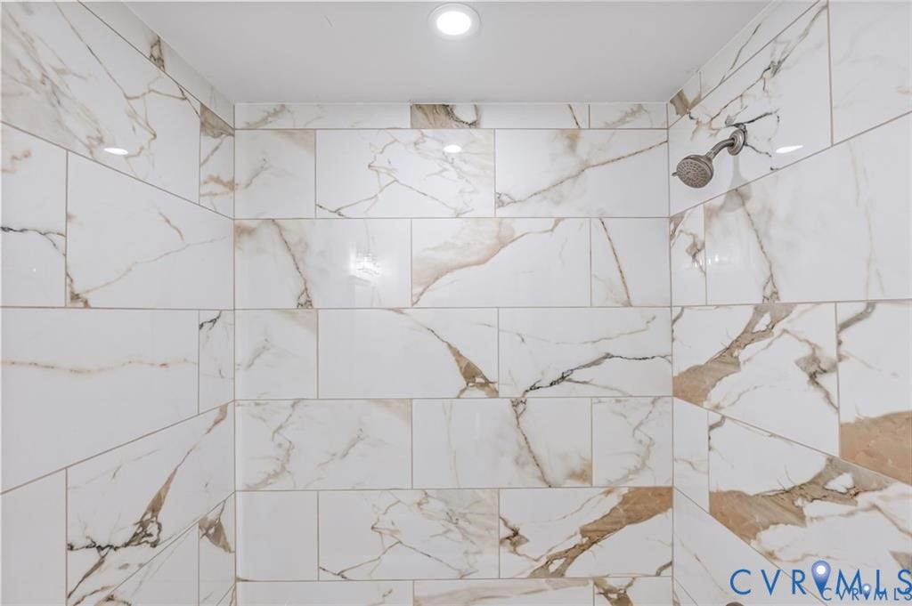 Shower enclosure featuring large format tile with natural stone-look veining, a ceiling-mounted recessed light, and a wall-mounted shower head