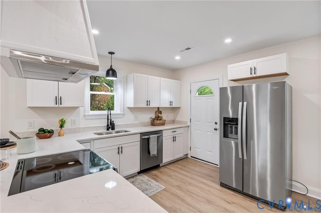Modern kitchen featuring white cabinetry, light-colored countertops, stainless steel appliances, and wood-finish flooring