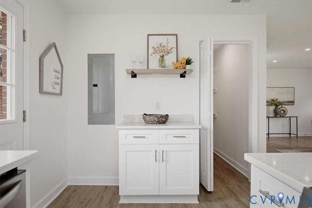 White shaker-style cabinetry with chrome hardware, light-toned countertops, wood-finish flooring, and a white paneled door