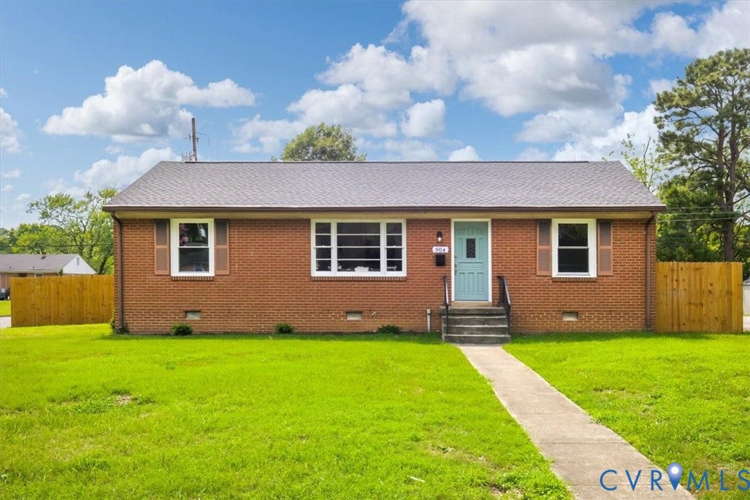 Brick exterior featuring a teal entry door with black hardware, white window frames, and brown shutters
