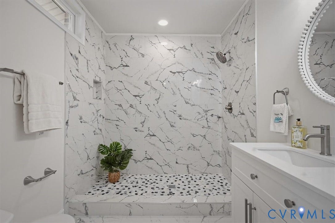Walk-in shower with marble-look wall tiling, pebble stone shower floor, built-in shower niche, and a rain shower head
