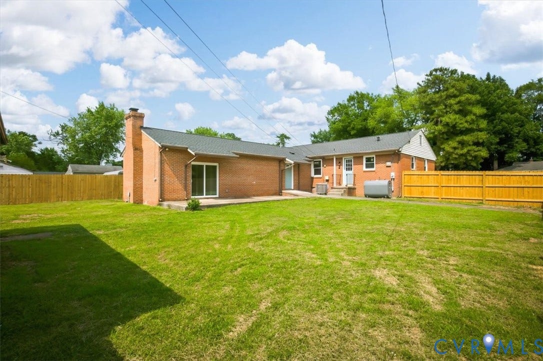 Expansive lawn with a wooden privacy fence, brick exterior, and a sliding glass patio door