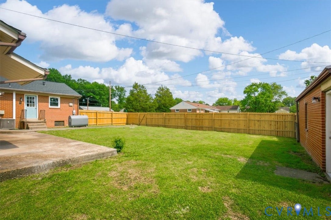 Expansive backyard with a manicured lawn, full privacy fencing, and a concrete patio