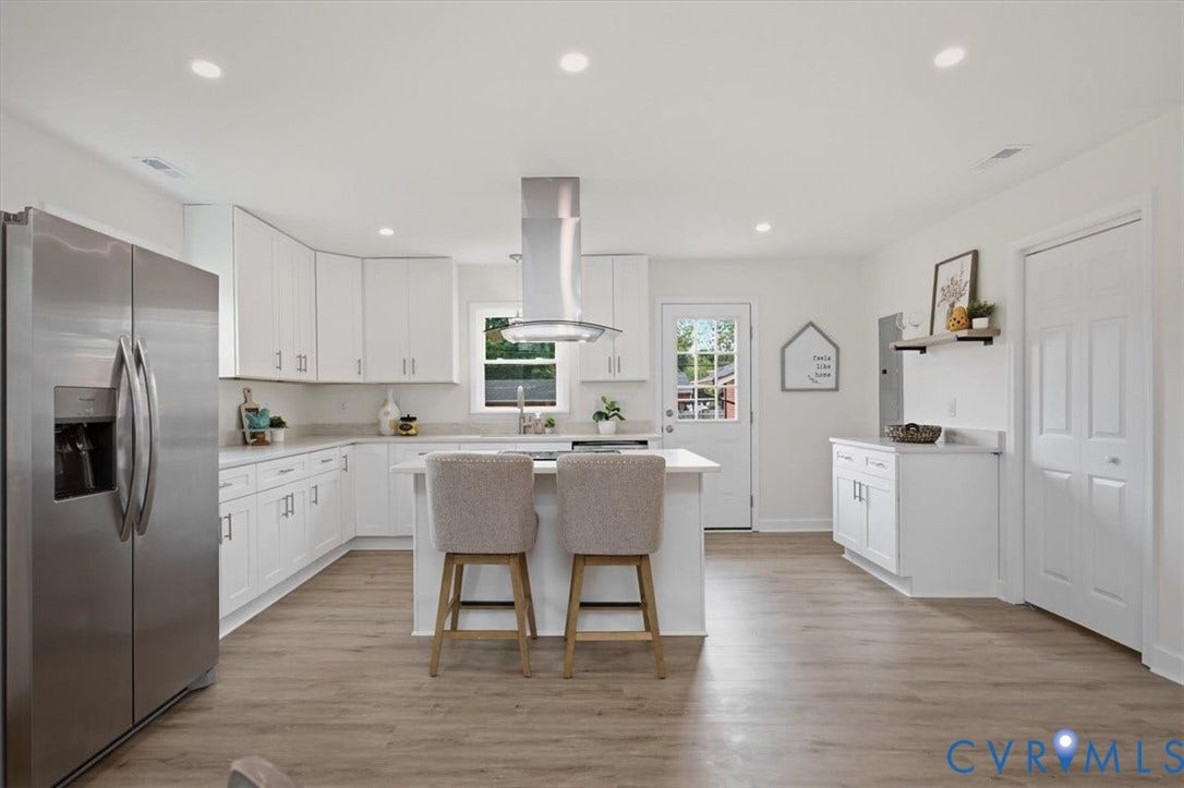 Bright kitchen featuring white cabinetry, stainless steel appliances, an island with countertop seating, wood-finish flooring, and recessed lighting