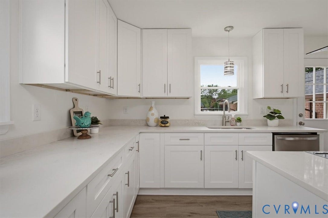 White shaker-style cabinetry, light-toned countertops, stainless steel sink with a modern faucet, wood-finish flooring, and a stainless steel dishwasher