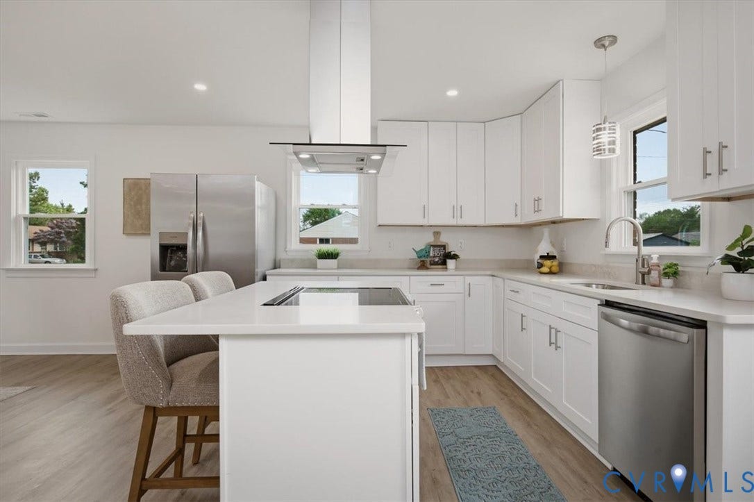 White cabinetry, wood-finish flooring, stainless steel appliances, central island with cooktop, and recessed lighting