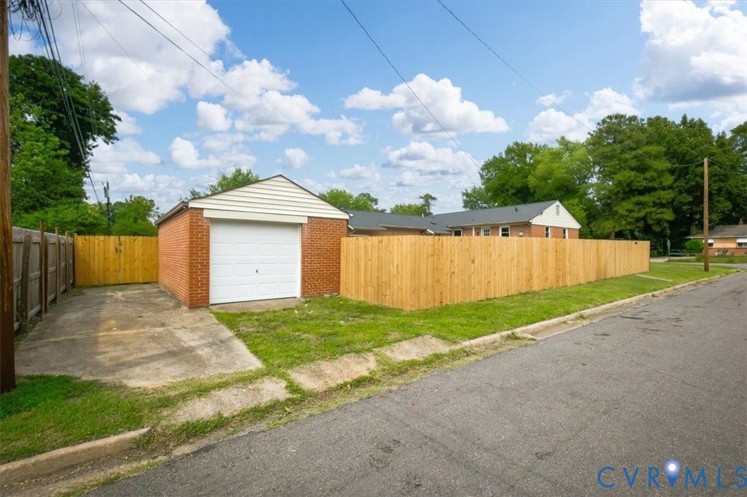 Detached brick garage with a white overhead door, concrete driveway, and a wooden privacy fence