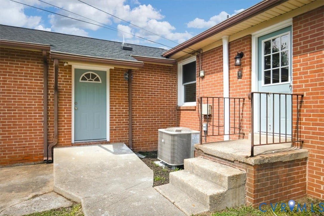 Brick exterior featuring two exterior entry doors, one with a concrete ramp and the other with concrete steps and a wrought iron railing