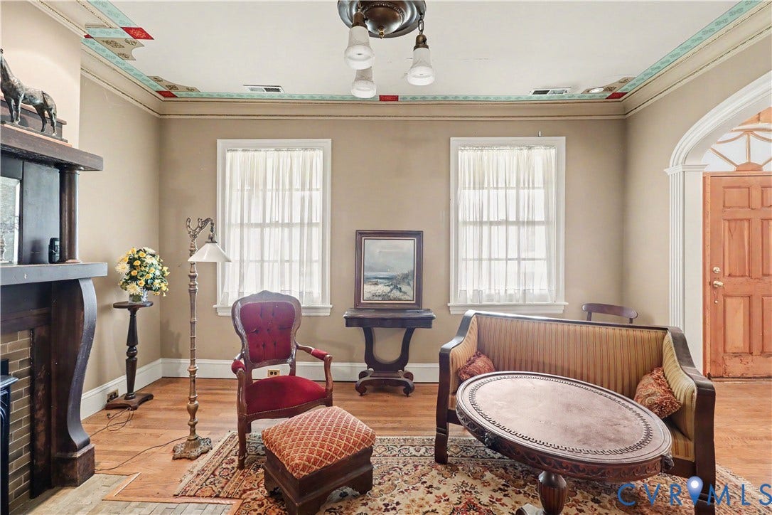 Hardwood flooring, decorative crown molding, fireplace with wooden mantel, arched doorway, and a ceiling fan with light fixture