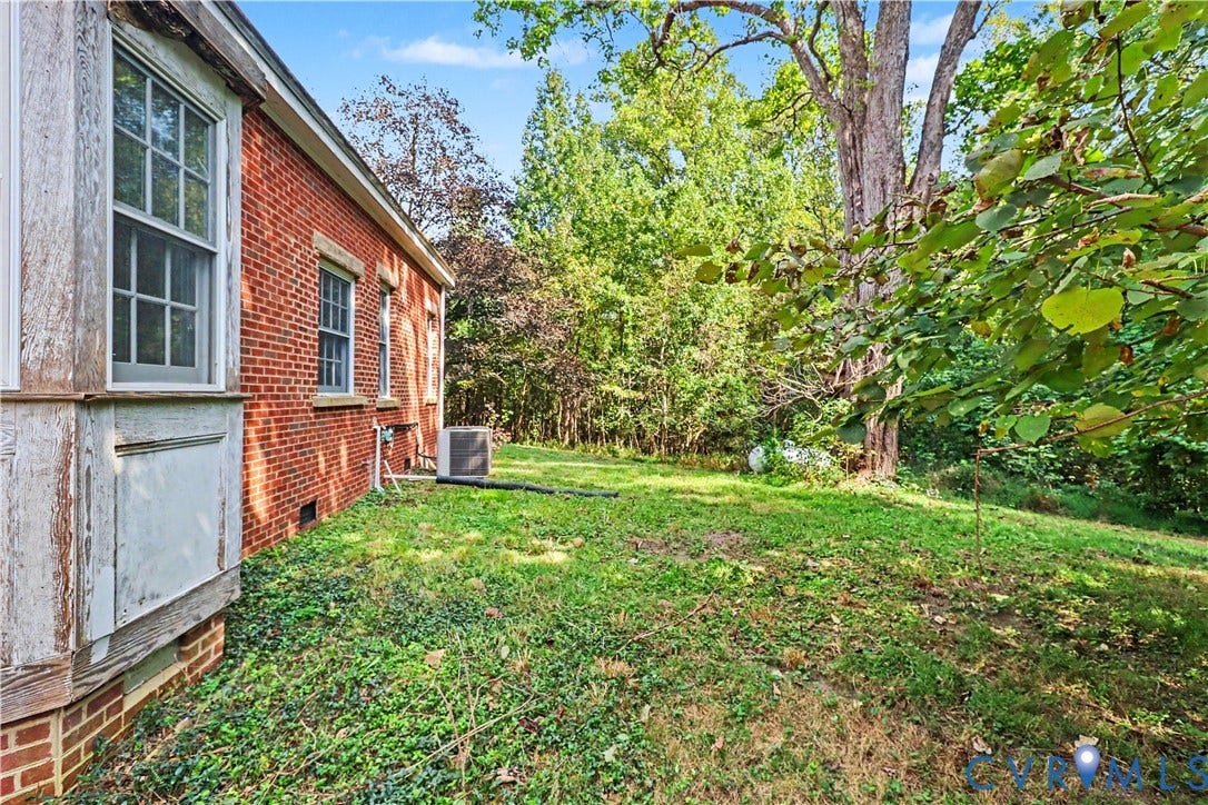 Red brick exterior with multiple windows, air conditioning unit, and lush green landscaping