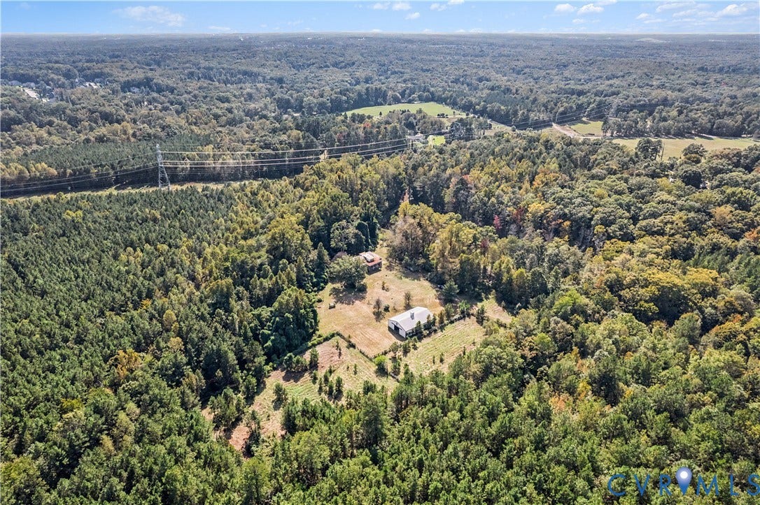 Expansive wooded acreage with a single-story dwelling, open cleared areas, and additional structures
