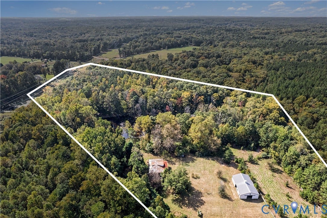Expansive wooded acreage with a substantial metal-roofed barn structure and a visible water feature