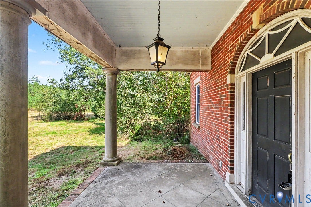 Brick exterior with a paneled entry door, arched transom window, covered porch, and concrete flooring