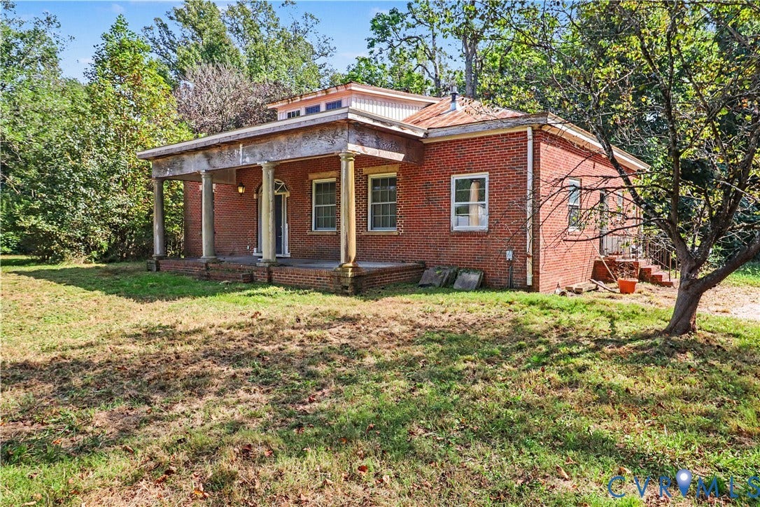 Red brick exterior with a columned front porch, a metal roof, and a visible rear entrance
