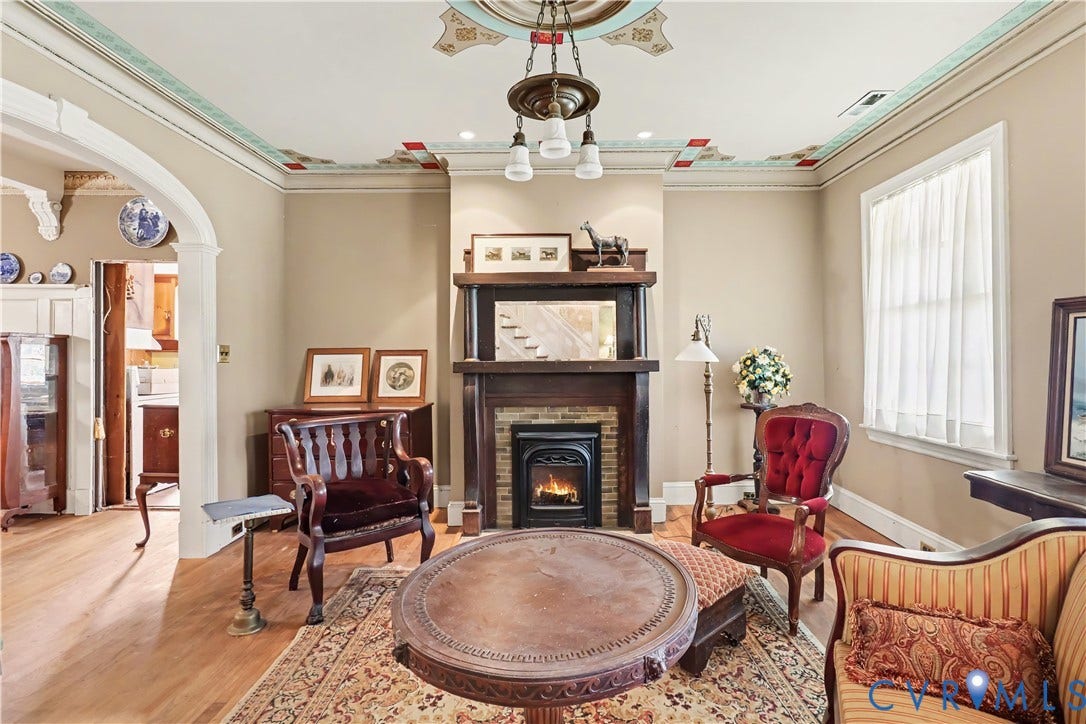Hardwood flooring, decorative ceiling details, ornate fireplace with mantel, arched doorway, and built-in lighting fixture