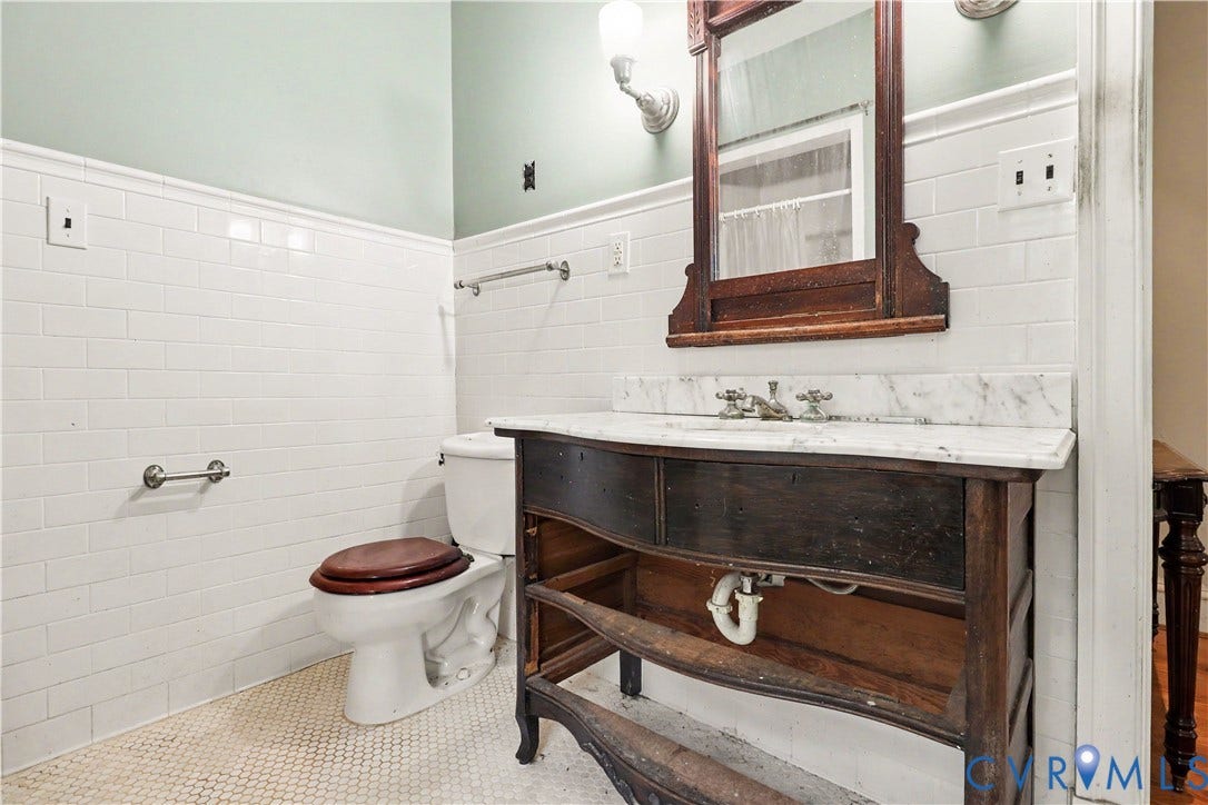 White subway tile wainscoting, decorative wood-framed mirror, vanity with stone countertop, and mosaic tile flooring