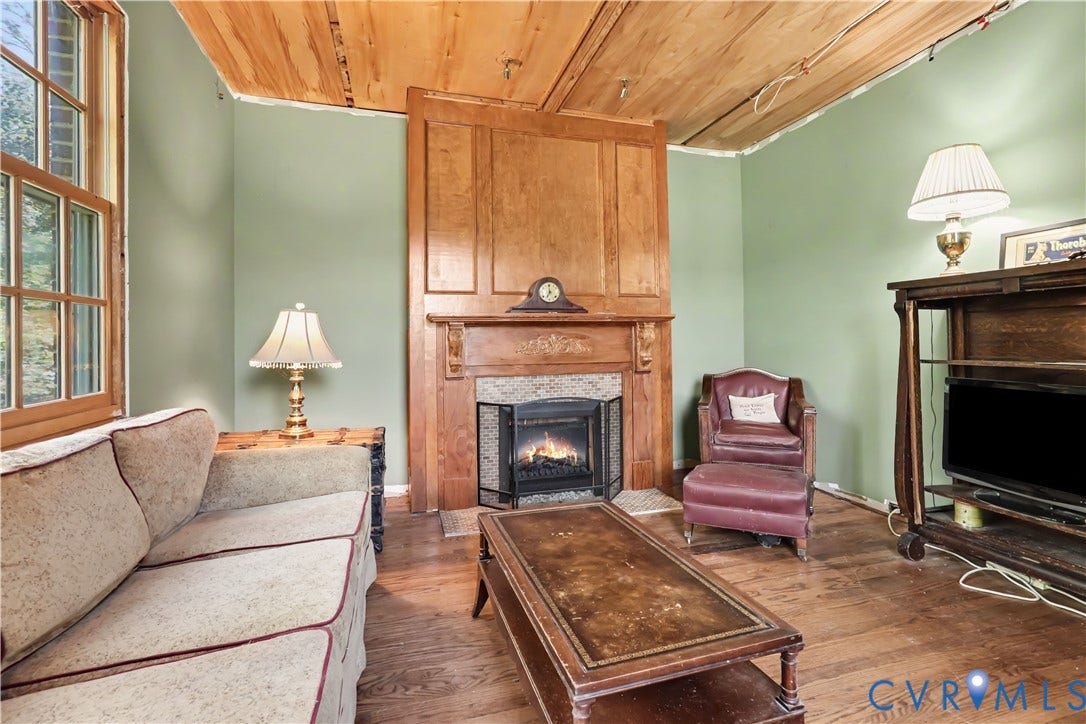 Hardwood flooring, wood-paneled ceiling, wood-framed windows, and a fireplace with a detailed wood surround