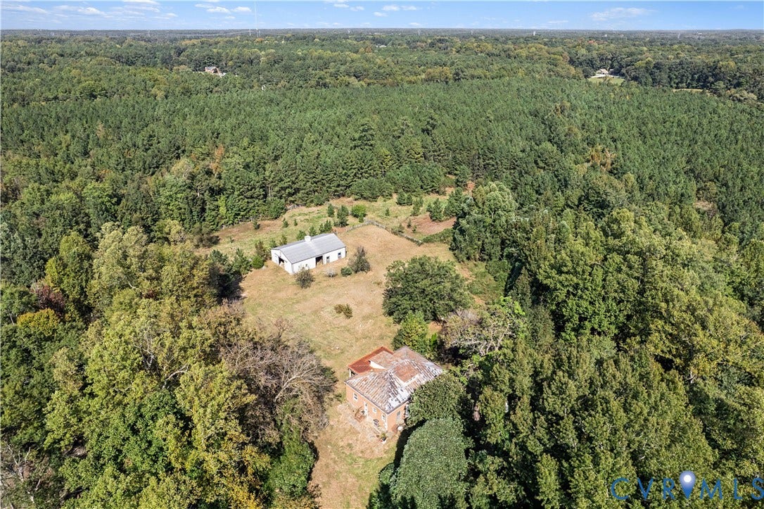 Aerial perspective showcasing substantial acreage, dense tree coverage, and two distinct structures