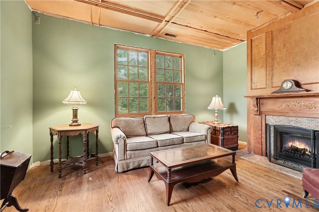 Hardwood flooring, wood-paneled walls, a fireplace with a tile surround, and exposed wood ceiling rafters