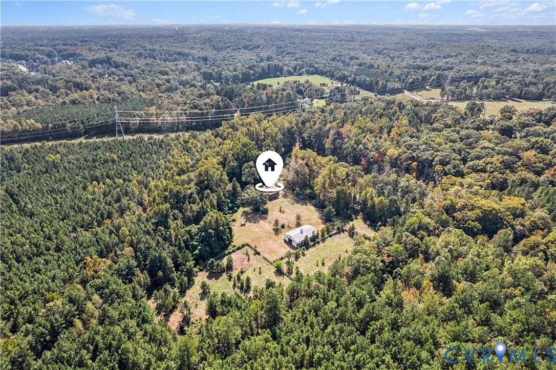 Expansive wooded property featuring a single-story residence with a light-colored roof, surrounded by cleared land