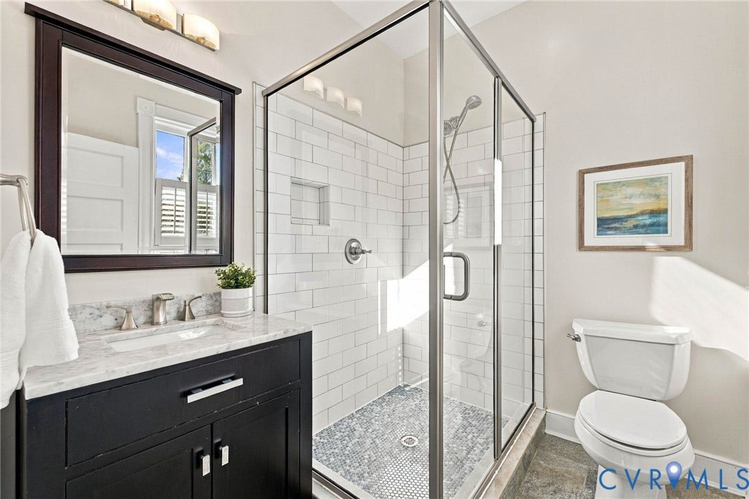 107 N Allen Avenue, The Fan, Richmond, VA 23220 Bathroom featuring a vanity with stone-top surfacing, a walk-in shower with white subway-style wall tile and a built-in recessed niche, a framed mirror with matching dark-finish cabinetry, and a glass shower enclosure with metallic framing