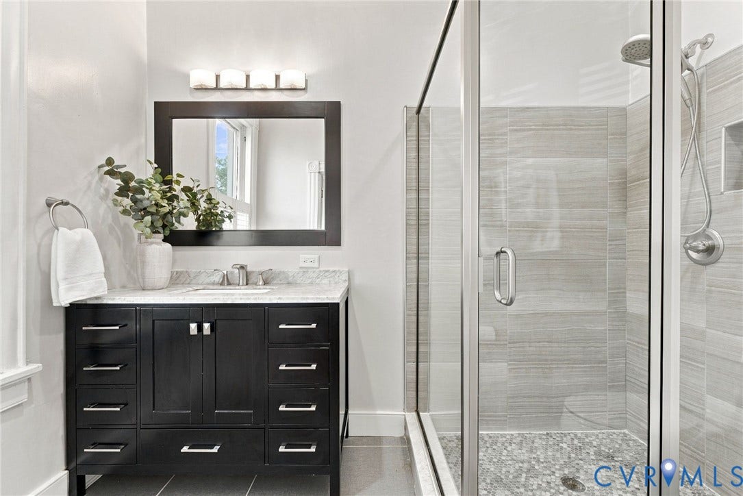107 N Allen Avenue, The Fan, Richmond, VA 23220 Dark wood-finish vanity with stone countertop, rectangular undermount sink, framed mirror with integrated lighting, and a glass-enclosed walk-in shower featuring horizontal wall tile and a stone-tiled basin