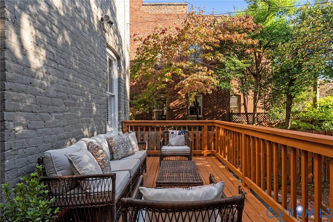107 N Allen Avenue, The Fan, Richmond, VA 23220 Elevated wooden deck featuring a stained finish, vertical baluster railing, painted brick exterior wall, and mature tree canopy