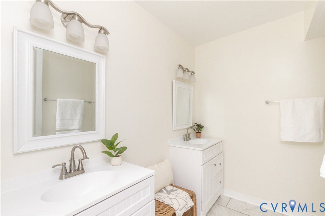 10404 Iron Mill Road, Chesterfield, VA 23235 Dual vanity setup featuring white cabinetry, integrated sinks, brushed nickel fixtures, and coordinating wall-mounted lighting.