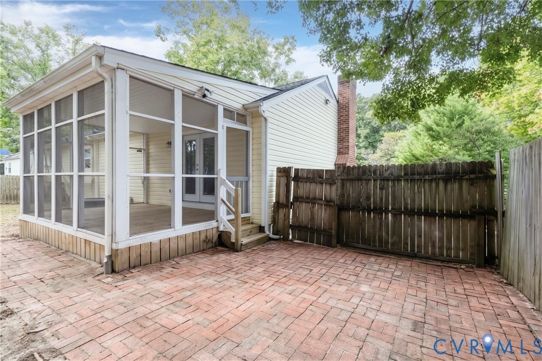 Spacious screened porch with wood-finish flooring, brick paver patio, wood privacy fence, and brick chimney