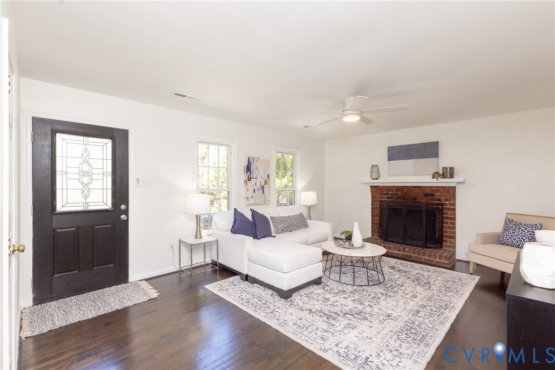 Dark wood-finish flooring, a brick-surround fireplace with a white mantel, and a ceiling fan with integrated lighting