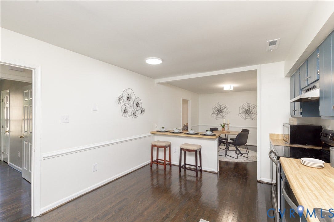 Rich wood-finish flooring, half-wall separation, light-toned wood countertops, recessed lighting, and blue upper cabinetry